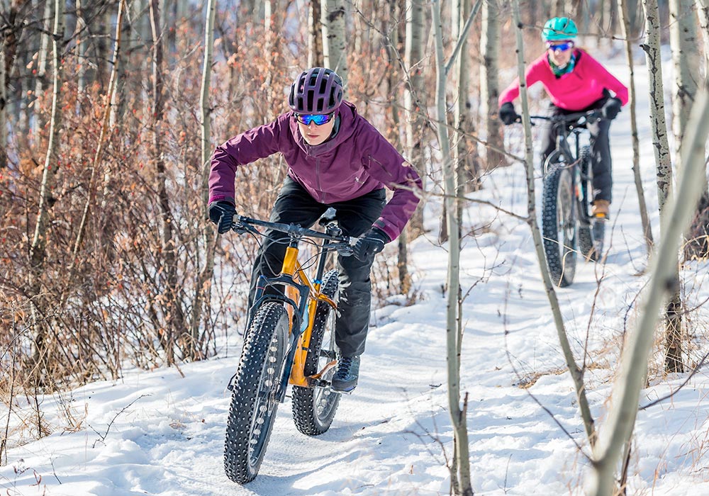 Two people fat tire biking on a trail through the woods