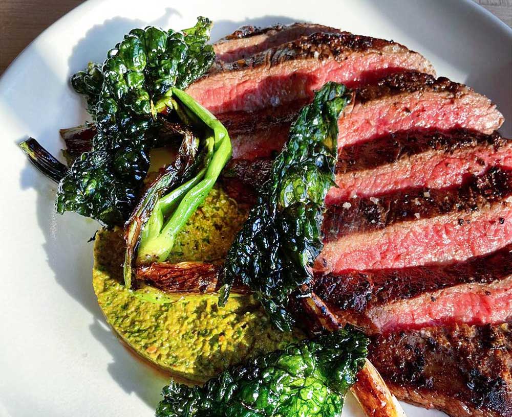 Plate of local flank, hazelnut tomatillo romesco, fried kale, grilled scallion at The Alna Store, Alna, Maine