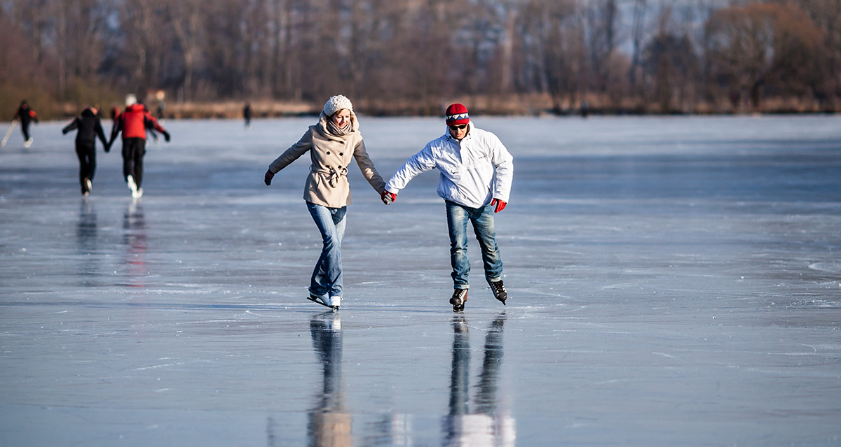 A couple ice skating outdoors on a frozen Maine pond